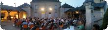 Une photo en fin de journée de la cour de la Mairie de Frozes. Un public très nombreux écoute les musiciens.